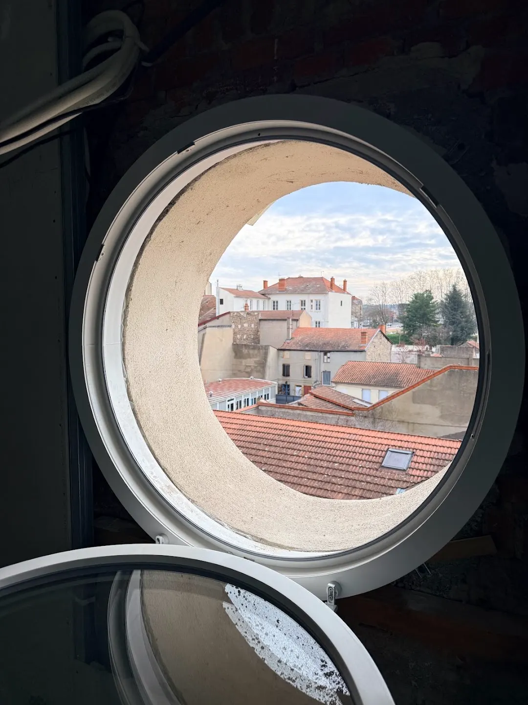 Vue sur les toits de Roanne à travers un œil-de-bœuf